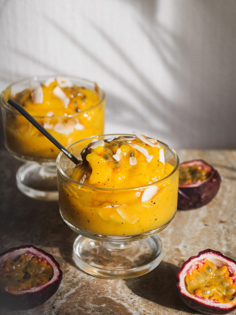 two glass dishes filled with Tropical Sunshine Sorbet surrounded by 3 fresh passion fruit halves