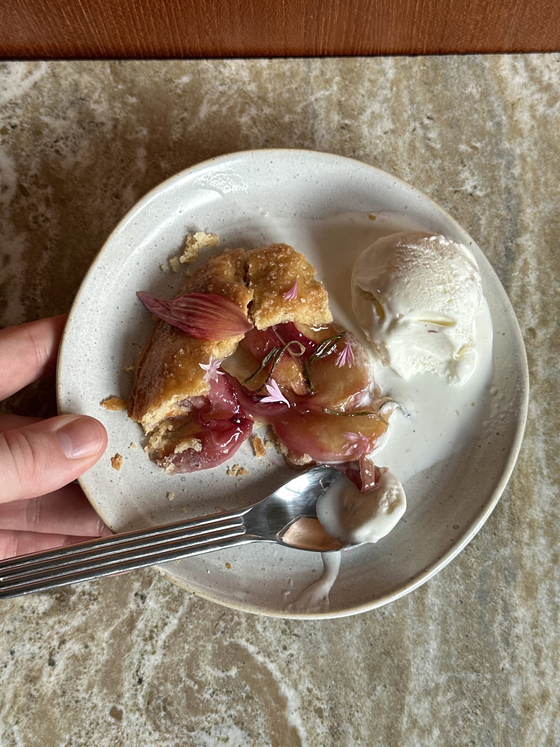 a plate with a slice of peach rosemary galette. edible flower garnish and a scoop of vanilla ice cream