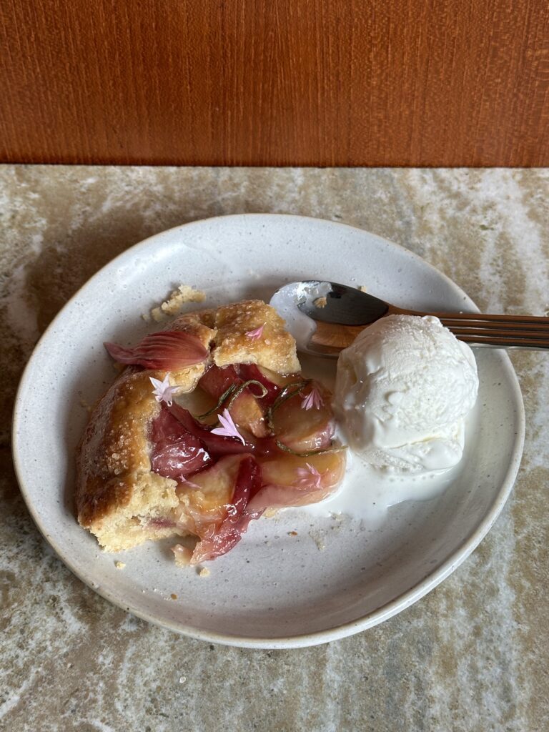 a slice of a peach rosemary galette with a scoop of vanilla ice cream